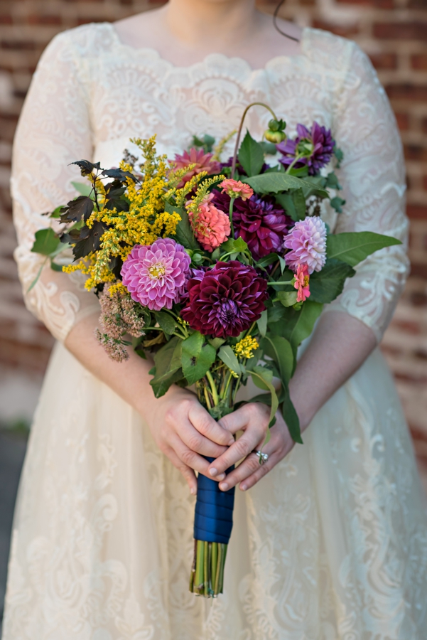 A colorful wedding bouquet in front of the brides lacy wedding dress.